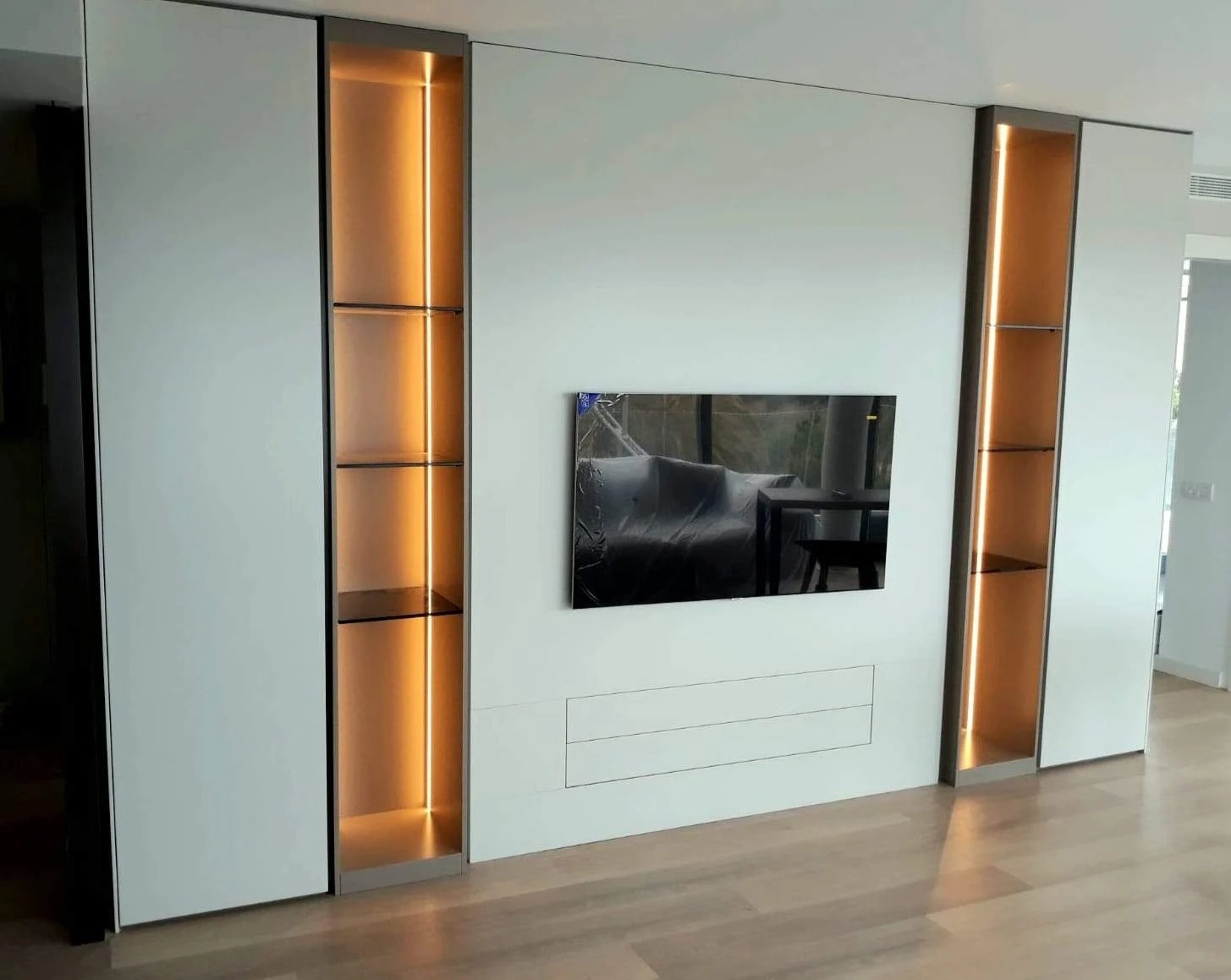 Composició de sala d’estar amb emmagatzematge, televisió central i prestatgeries il·luminades.